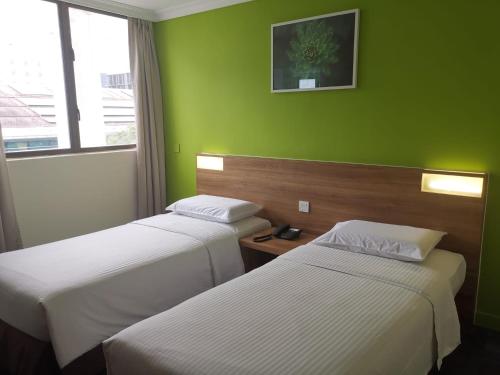 two beds in a hotel room with green walls at YMCA One Orchard in Singapore