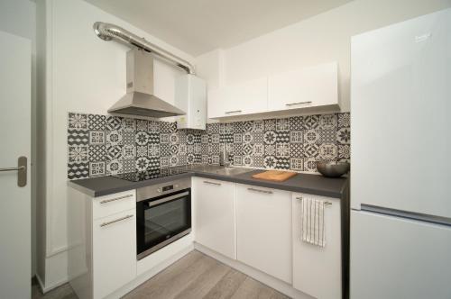 une cuisine avec des armoires blanches et un four à plaques de cuisson dans l'établissement Appartement tout équipé parking balcon 2 chambres, à Marseille