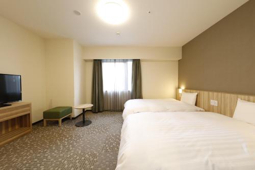 a hotel room with two beds and a flat screen tv at Dormy Inn Maebashi in Maebashi