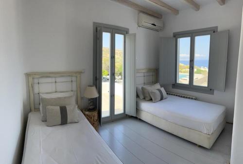 Villa Amarone في مدينة ميكونوس: سريرين في غرفة بيضاء مع نوافذ