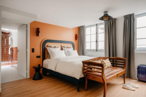 a bedroom with a bed and a bench and windows at Edgar Suites Louvre - Jour in Paris