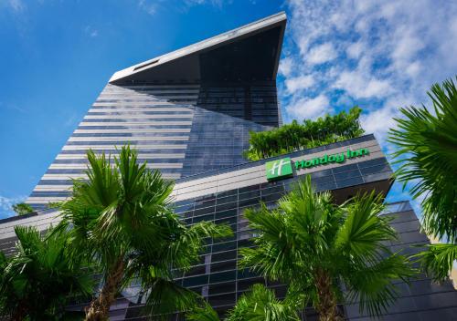 a building with a sign in front of palm trees at Holiday Inn Bangkok Sukhumvit, an IHG Hotel in Bangkok