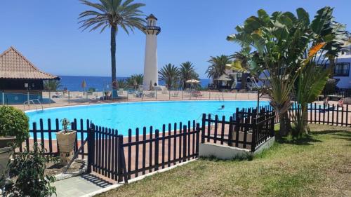 a fence around a swimming pool with palm trees and the ocean at Sun club playa del águila by la piedra viva in San Bartolomé