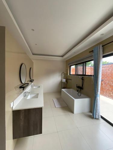 La salle de bains est pourvue d'un lavabo, d'une baignoire et d'une fenêtre. dans l'établissement Exclusive Farm Getaway, à Lusaka