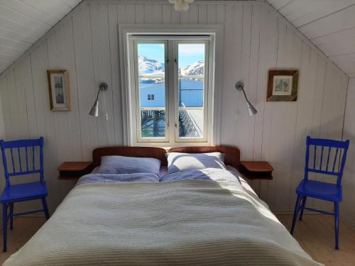 a bed in a room with two blue chairs and a window at Lovisenborg Brygge in Kongsfjord
