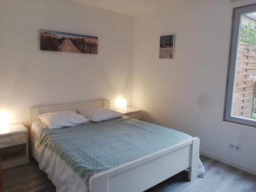 a white bedroom with a bed and two night stands at Maison moderne proche lac et plage in Léon
