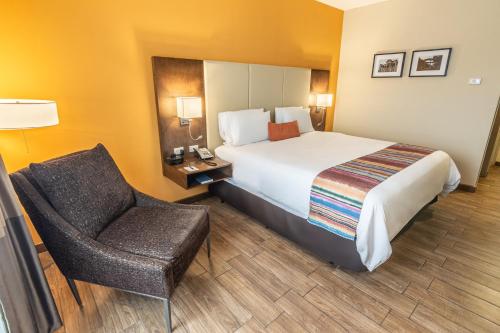 a hotel room with a bed and a chair at LATAM HOTEL Plaza Pradera Quetzaltenango in Quetzaltenango