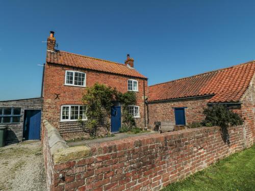 a brick house with blue doors and a brick wall at Bellafax Cottage in Kirby Misperton