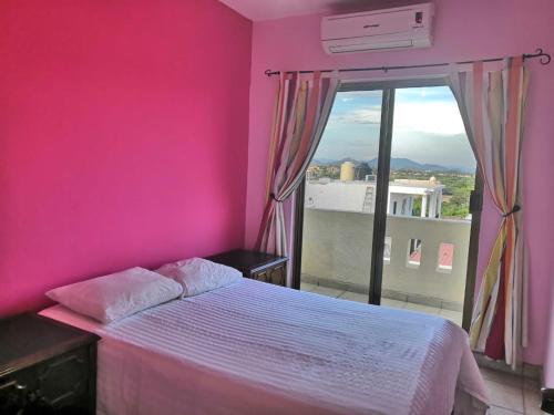 ein Schlafzimmer mit einer rosa Wand und einem Bett mit einem Fenster in der Unterkunft Garimar Condominios en San Carlos in San Carlos