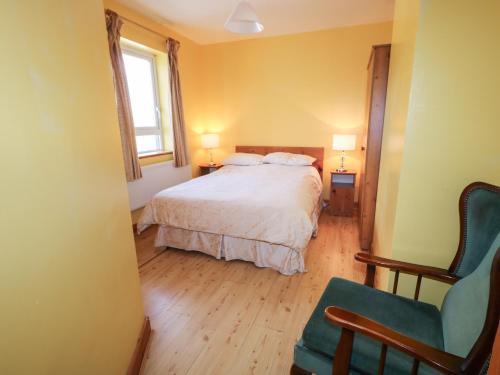 a bedroom with a bed and a chair and a window at Carnmore Cottage in Dungloe