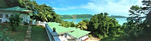a house with a green roof next to a body of water at Seychelles Yellow Petals in Anse Boileau