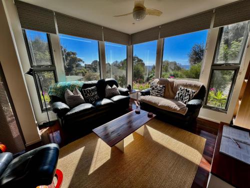 a living room with couches and a table and windows at Sunrise on Falie Seaview Eco Accommodation in American River