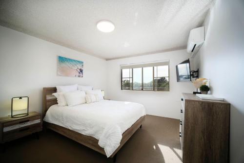 ein weißes Schlafzimmer mit einem Bett und einem Fenster in der Unterkunft Oceancrest 12 Pebbly Beach in Forster