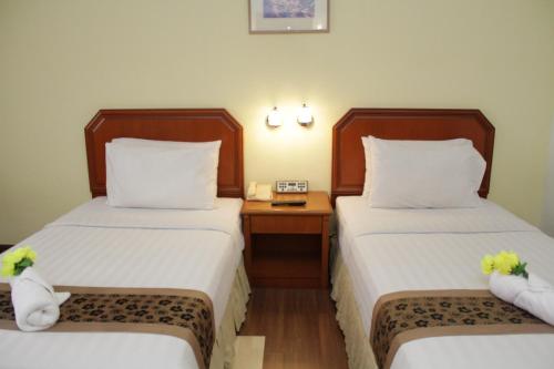 a hotel room with two beds and a night stand at Hotel Sandakan in Sandakan