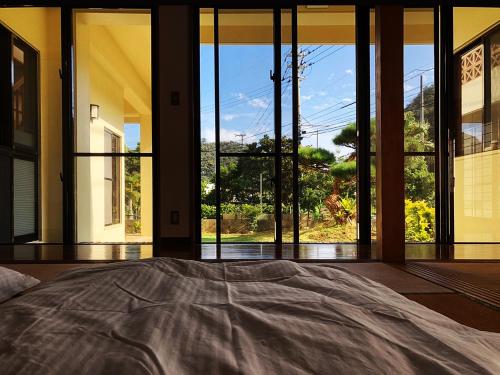 un letto in una camera con ampie vetrate di やんばる別荘三原でーじまぎー -Yanbaru stay MIHARA VILLA GRANDE- a Nago