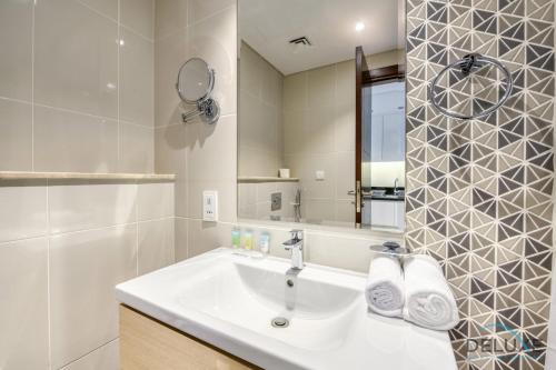 a white bathroom with a sink and a mirror at Sunlit Studio at Golf Promenade 2A DAMAC Hills By Deluxe Holiday Homes in Dubai
