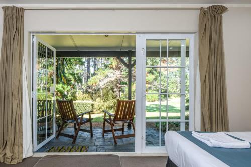 a bedroom with a bed and two chairs on a porch at Northridge Golf Resort in Orewa
