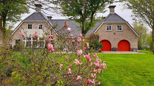 een huis met een rode deur en wat roze bloemen bij B&B Hoptille in Hijlaard