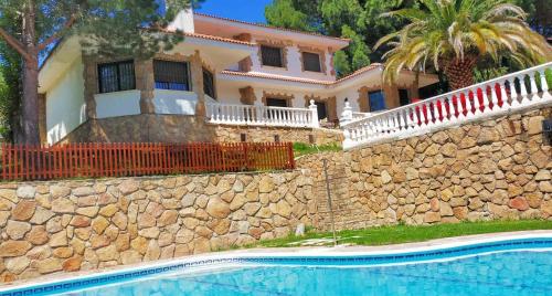 een huis en een zwembad voor een stenen muur bij Casa Blanca de La Sierra hasta 24 hasta personas con Piscina Salina y Bbq in Pelayos de la Presa
