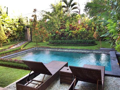 a swimming pool with two chairs and a table at Villa D'Uma in Ubud