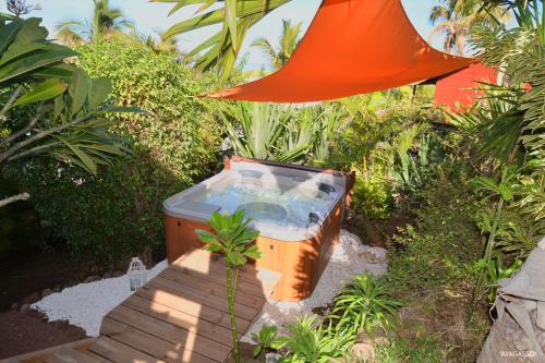 a hot tub in a garden with an orange umbrella at Poz Lagon in La Saline les Bains