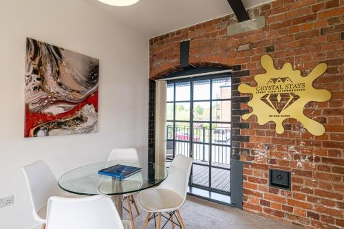 a dining room with a brick wall and a glass table and chairs at Clock Towers, 2 Bed, Stockton Heath, Warrington, Parking in Warrington