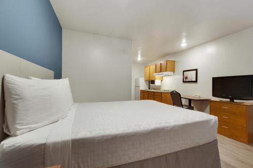 a bedroom with a white bed and a television at WoodSpring Suites Houston Westchase in Houston