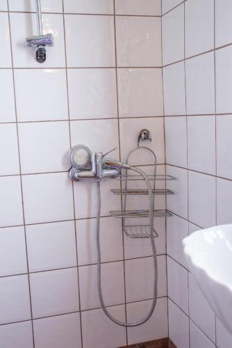 a shower in a white tiled bathroom with a hose at Sunray Luxury Apartment Zagora with piano in Zagora