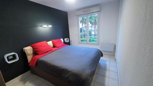 Schlafzimmer mit einem Bett mit roten Kissen und einem Fenster in der Unterkunft L'Atalante, 2 pièces 47m2 rénové résidence piscine in Villeneuve-Loubet