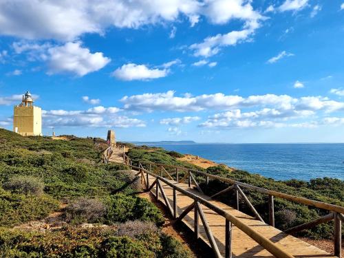 a lighthouse on a hill next to the ocean with a wooden bridge at Apartamentos El Arrecife in Conil de la Frontera