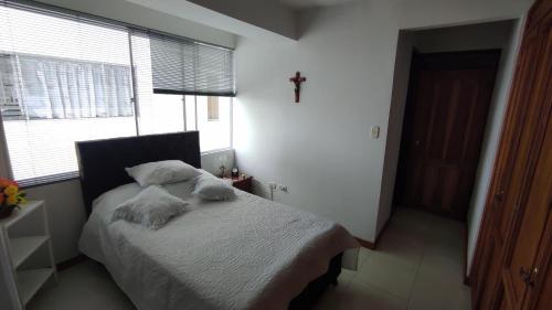 1 dormitorio con 1 cama con sábanas blancas y una cruz en la pared en APARTAMENTO CÓMODO, ILUMINADO Y CENTRAL EN MANIZALES en Manizales