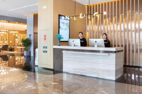 two people sitting at a counter in a lobby with laptops at Atour Hotel Korla in Korla