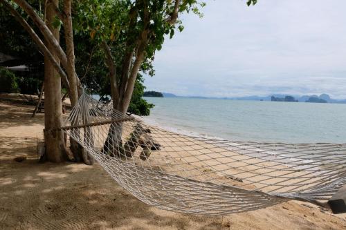 a hammock on a beach next to the water at Touch Glamping Koh Yao Noi ทัช แกรมปิ้ง เกาะยาวน้อย in Ko Yao Noi