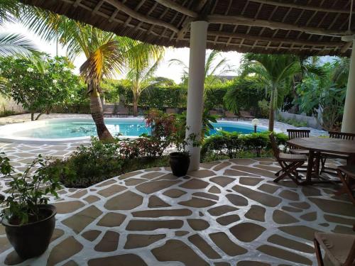 瓦塔穆Twiga House Resort [ Piscina ☆☆☆☆☆ ] Pearl Beach的带桌椅和游泳池的露台