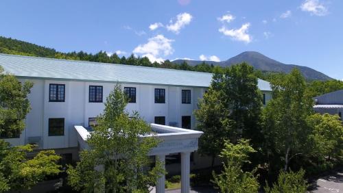 a white building with trees and mountains in the background at Tabist Hotel Colosseum Inn Tateshina in Tateshina