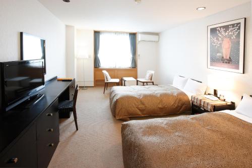 a hotel room with two beds and a flat screen tv at Tabist Hotel Colosseum Inn Tateshina in Tateshina