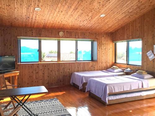 two beds in a room with wooden walls and windows at Minshuku Yadokari in Zamami