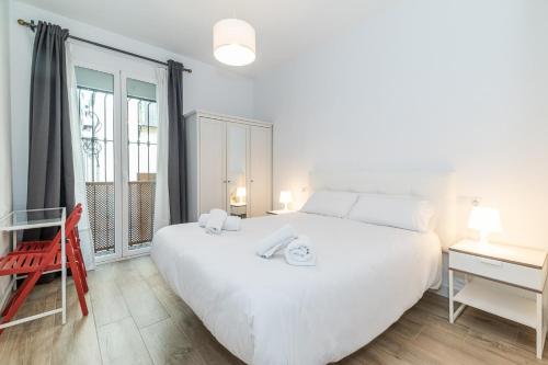 a white bedroom with a large white bed and a window at Céntrico y tranquilo apartamento Realejo in Granada