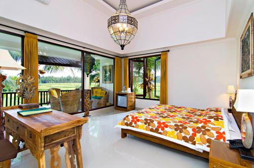 a bedroom with a bed and a desk and windows at Green Field Hotel and Restaurant in Ubud