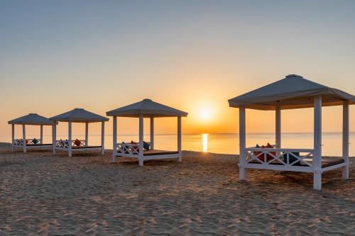 three beds on a beach with the sunset in the background at Sealine Beach, a Murwab Resort in Mesaieed
