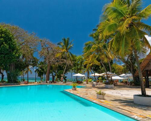 a swimming pool with palm trees and a beach at Safari Beach Hotel in Diani Beach