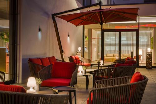 a patio with chairs and a red chair and an umbrella at IntercityHotel Zürich Airport in Rümlang