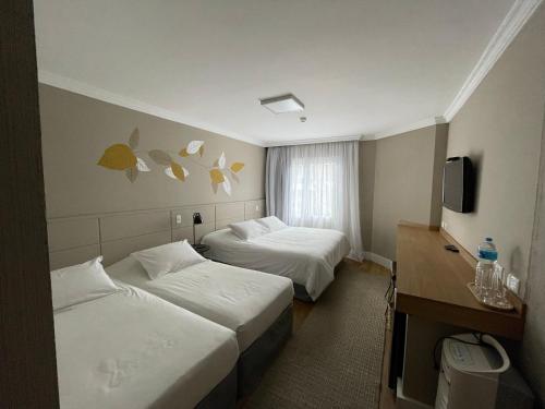 a hotel room with two beds and a television at Pousada Telhado de Ouro in Campos do Jordão