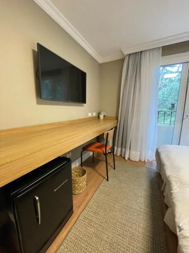 a hotel room with a desk with a television on the wall at Pousada Telhado de Ouro in Campos do Jordão