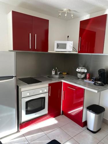 une petite cuisine avec des placards rouges et un four micro-ondes dans l'établissement Appartement proche de la plage, à Saint Pierre La Mer