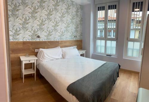 a bedroom with a bed and a table and two windows at Aloha Hostel in Pamplona