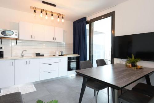 a kitchen with white cabinets and a table and a television at YalaRent Migdalor Apartments with Sea Views Tiberias in Tiberias