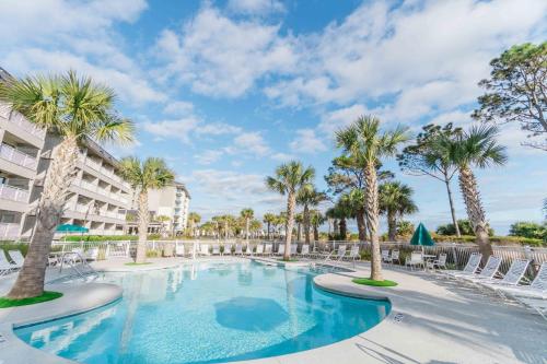 a large swimming pool with palm trees and chairs at Stunning Views!!-Oceanfront Villa-Heated Pool-Private Balcony-Tiki Bar-Walk to Coligny Plaza in Hilton Head Island