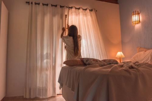 a woman is looking out the window of a bedroom at Pousada Areias do Rosa in Praia do Rosa