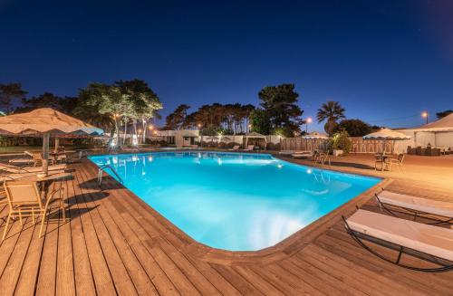 a swimming pool at night with chairs and umbrellas at Hotel Vale Da Telha in Aljezur